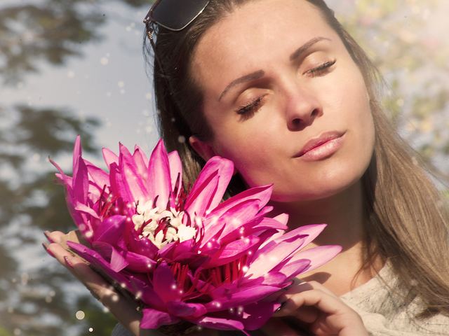 Frau mit geschlossenen Augen und einer pinkfarbenen Blüte